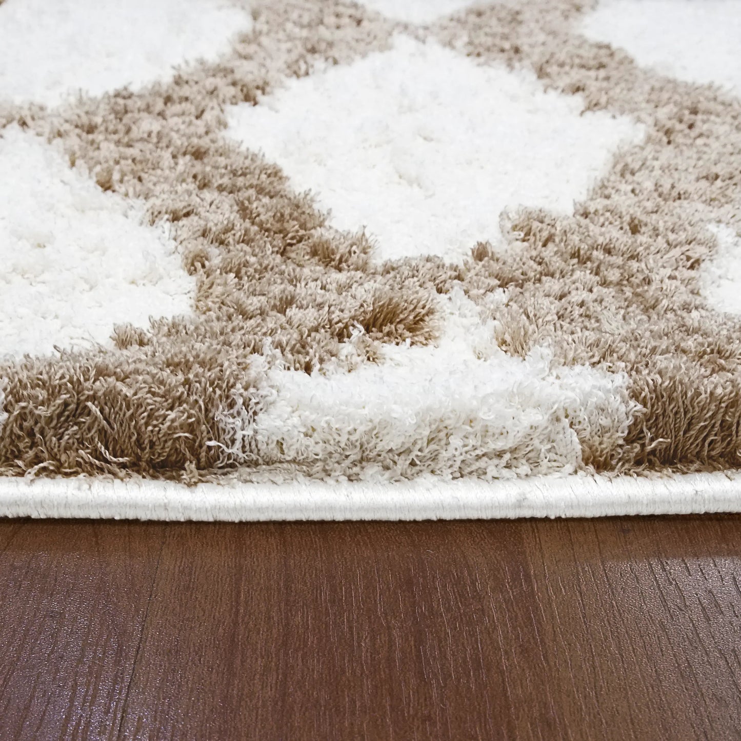 A closeup of rectangular rug with a contemporary geometric pattern in beige and white shades, featuring a plush microfiber pile.