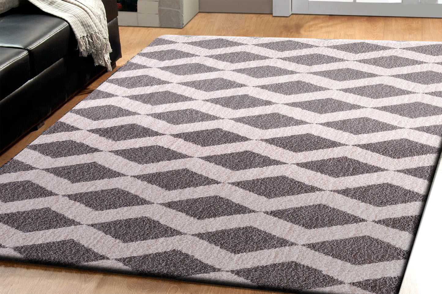 A rectangular rug with a contemporary geometric pattern in beige and brown shades, featuring a plush microfiber pile on a wooden floor.