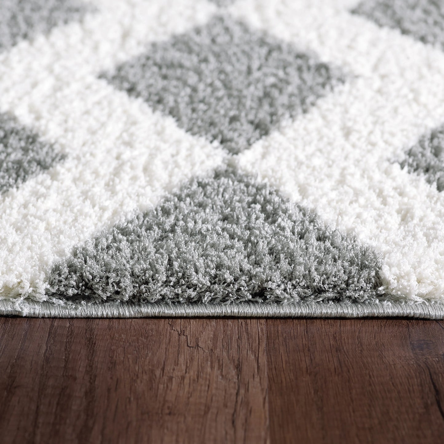 A closeup of rectangular rug with a contemporary geometric pattern in white and grey shades, featuring a plush microfiber pile.