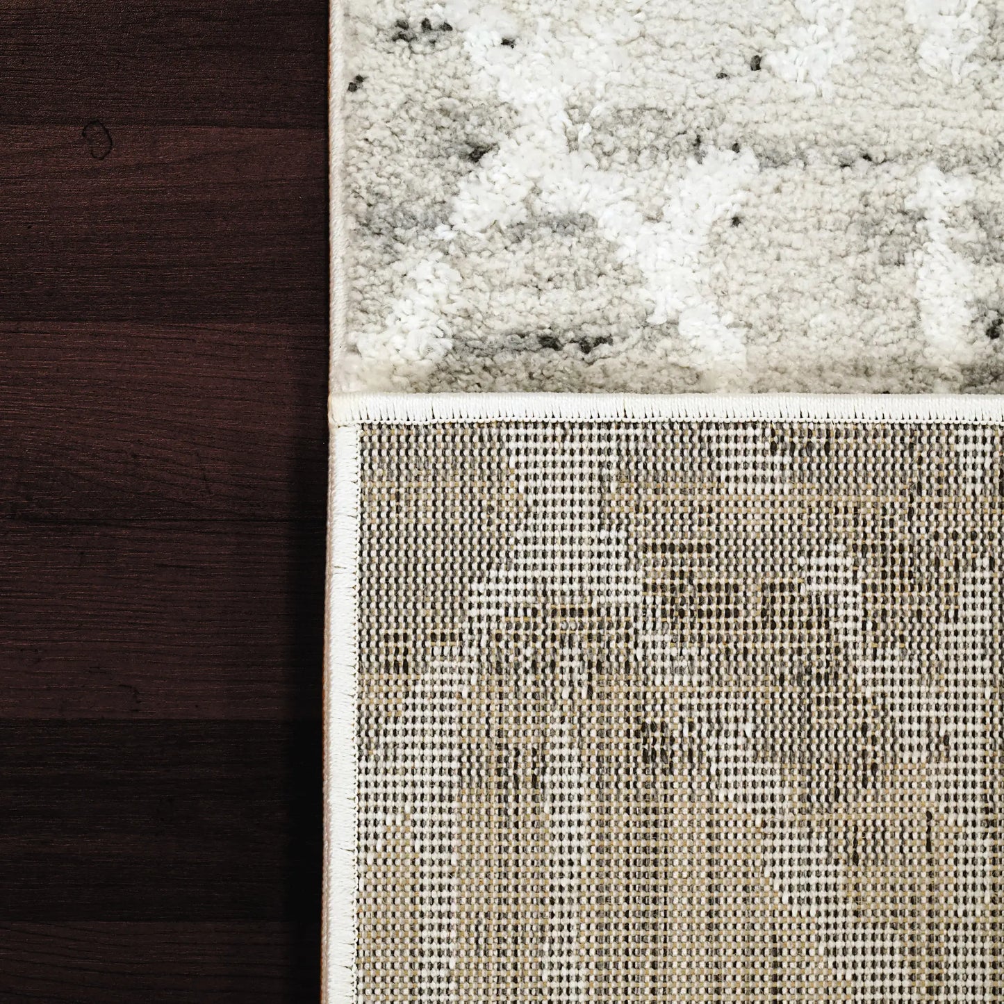 A rectangular rug in a grey ivory color palette against a dark wooden floor.