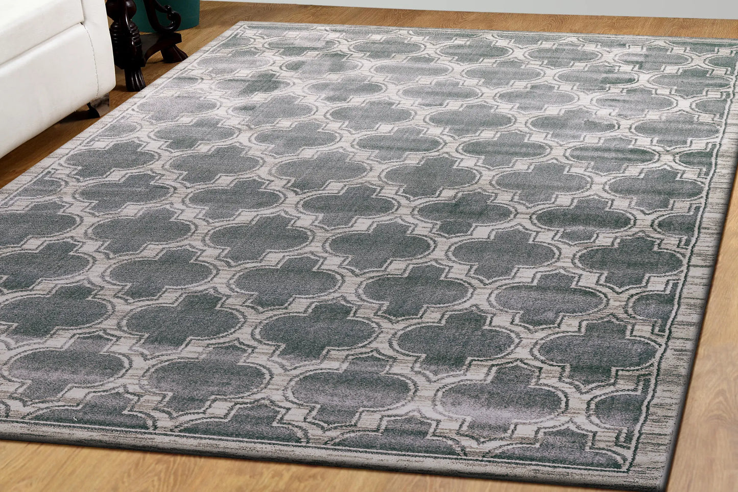 A rectangular traditional wool rug with a geometric pattern in grey and ivory colors on a wooden floor.