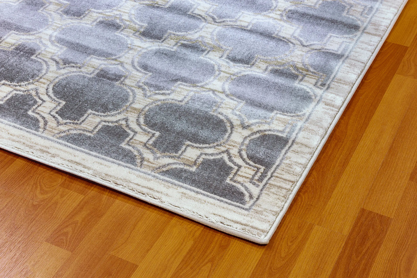 The closeup edge of a rectangular traditional wool rug with a geometric pattern in grey and ivory colors.